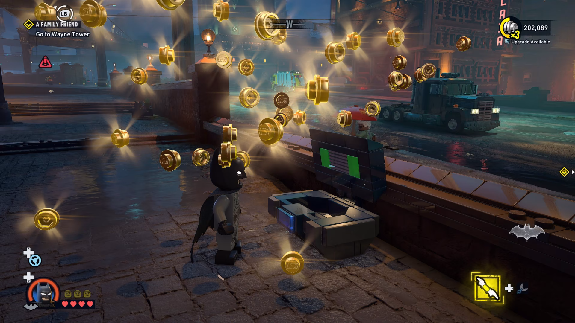 A LEGO Batman: Legacy of the Dark Knight character collects golden LEGO coins next to a screen, with objectives to 'Go to Wayne Tower' displayed in the top left.